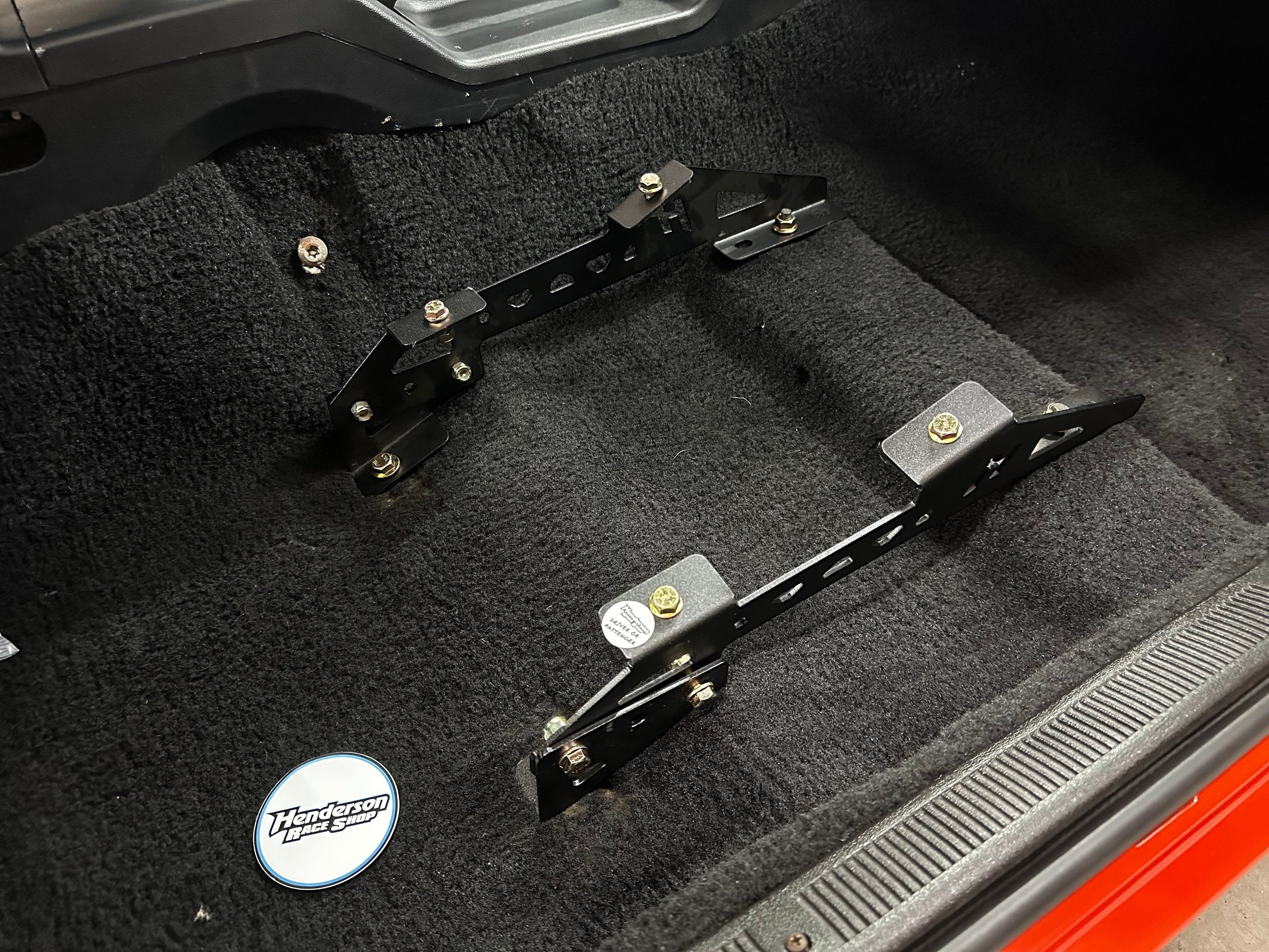 Henderson Race Shop Store black steel seat mount brackets installed on the carpeted floor of a Ford Mustang.