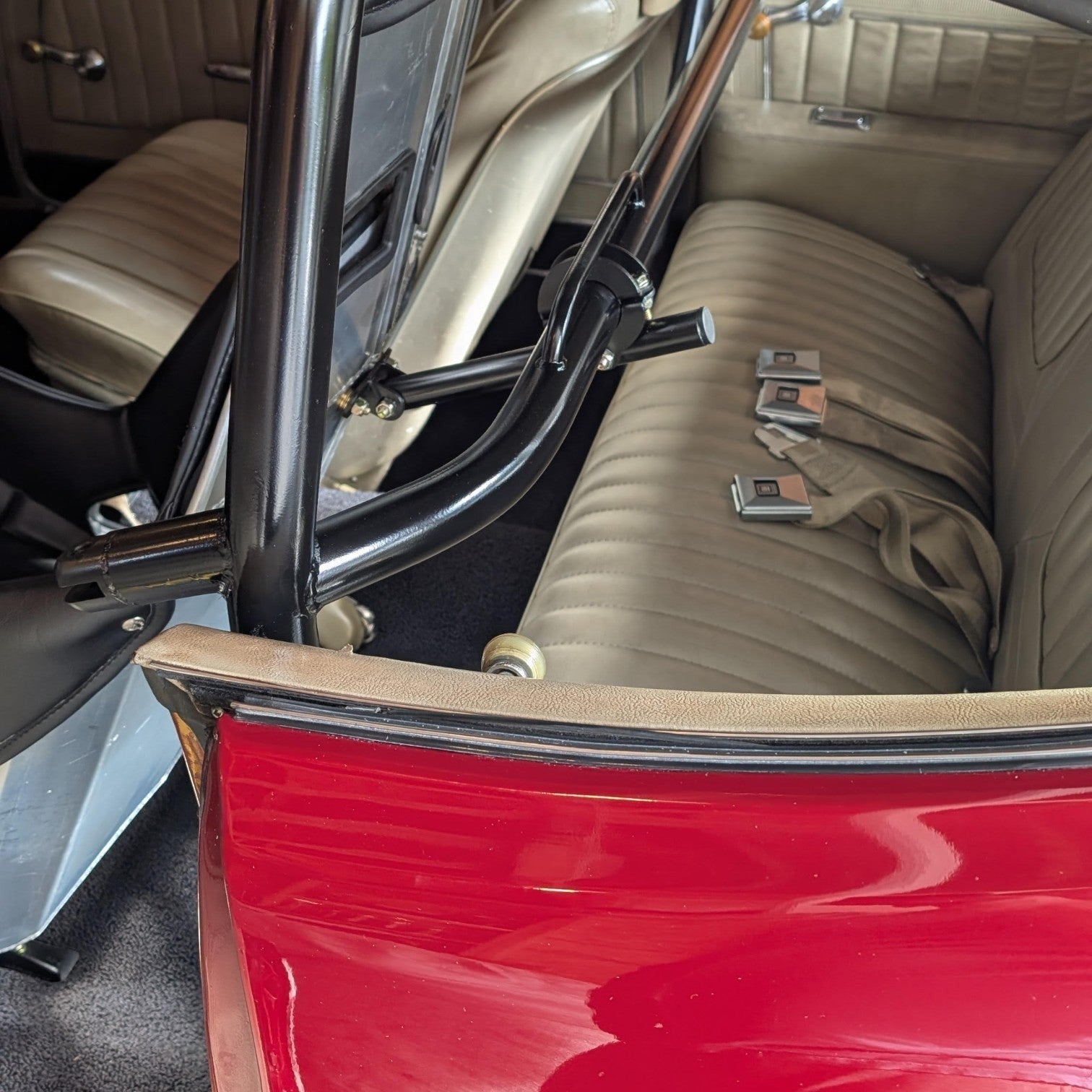 Henderson Race Shop Store bolt-on seat back brace installed on a harness bar in a red vehicle interior