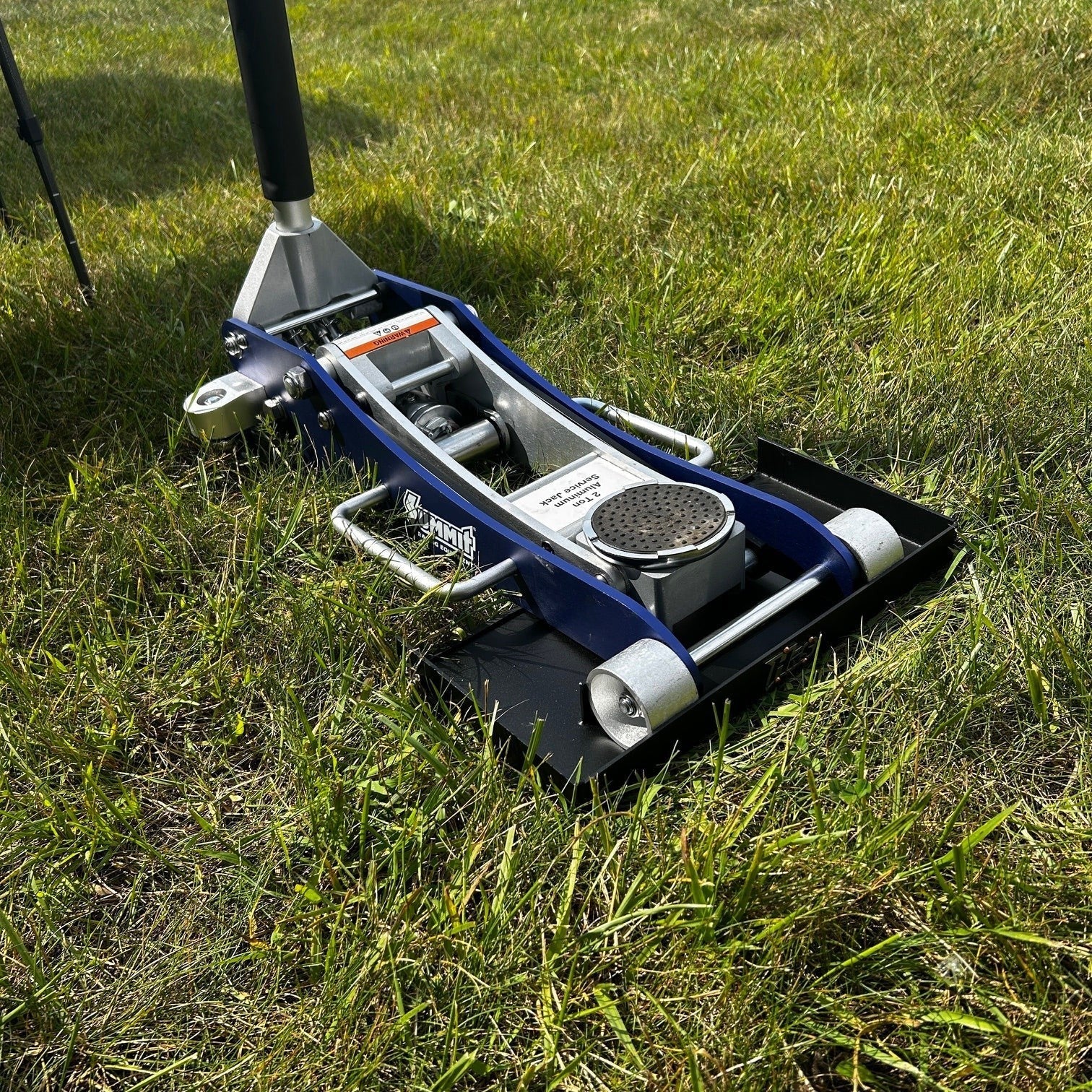 Henderson Race Shop Store floor jack pad under a blue aluminum jack on grass for stable lifting on soft surfaces
