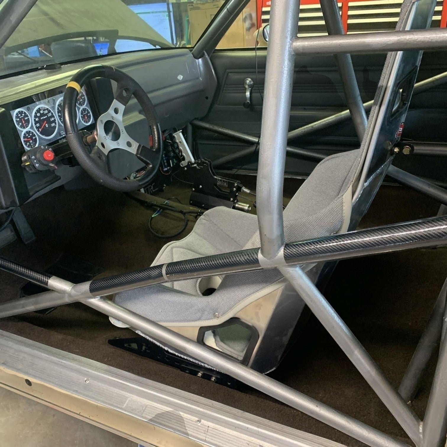 Henderson Race Shop Store seat mounts installed under a grey Kirkey racing seat in a G-Body vehicle with a roll cage.