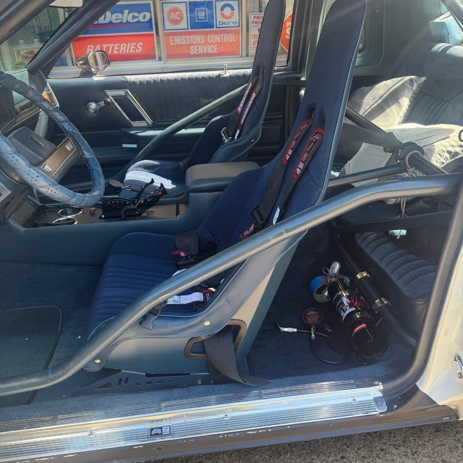 Henderson Race Shop Store seat mounts installed under a blue racing seat in a GM G-Body vehicle interior