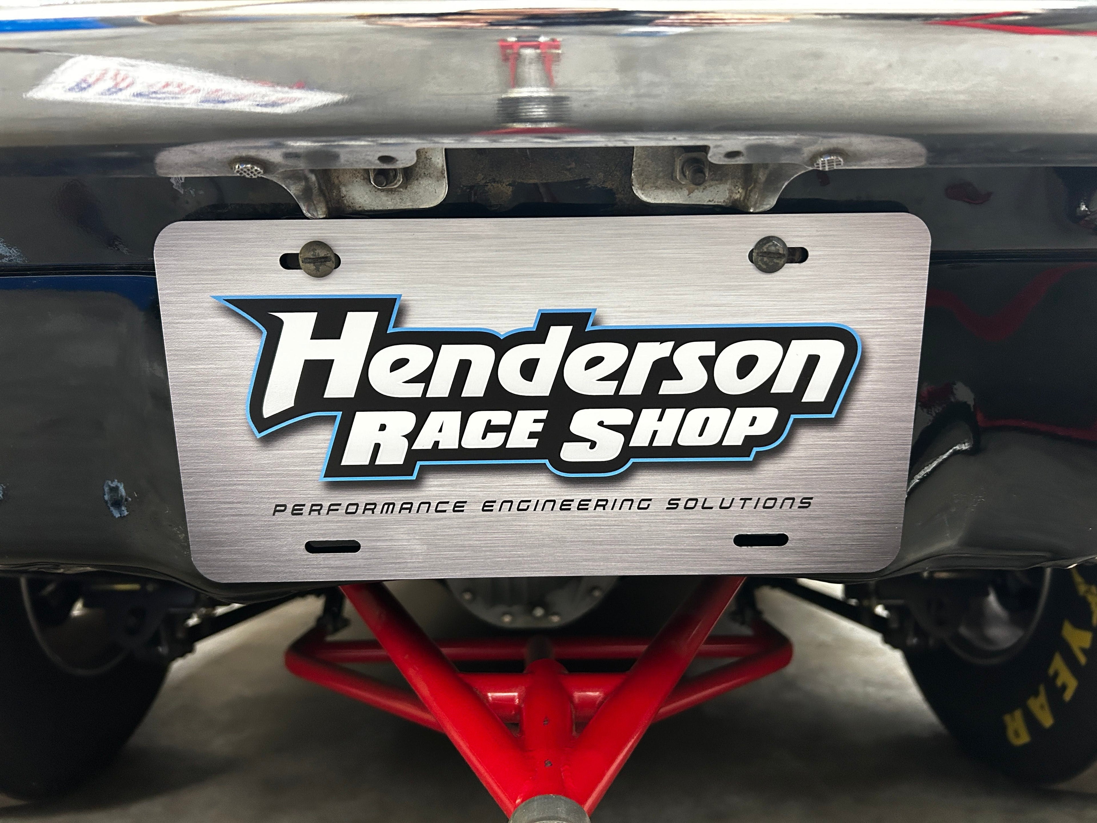 Henderson Race Shop Store metal license plate with laser-printed logo mounted on a race car bumper