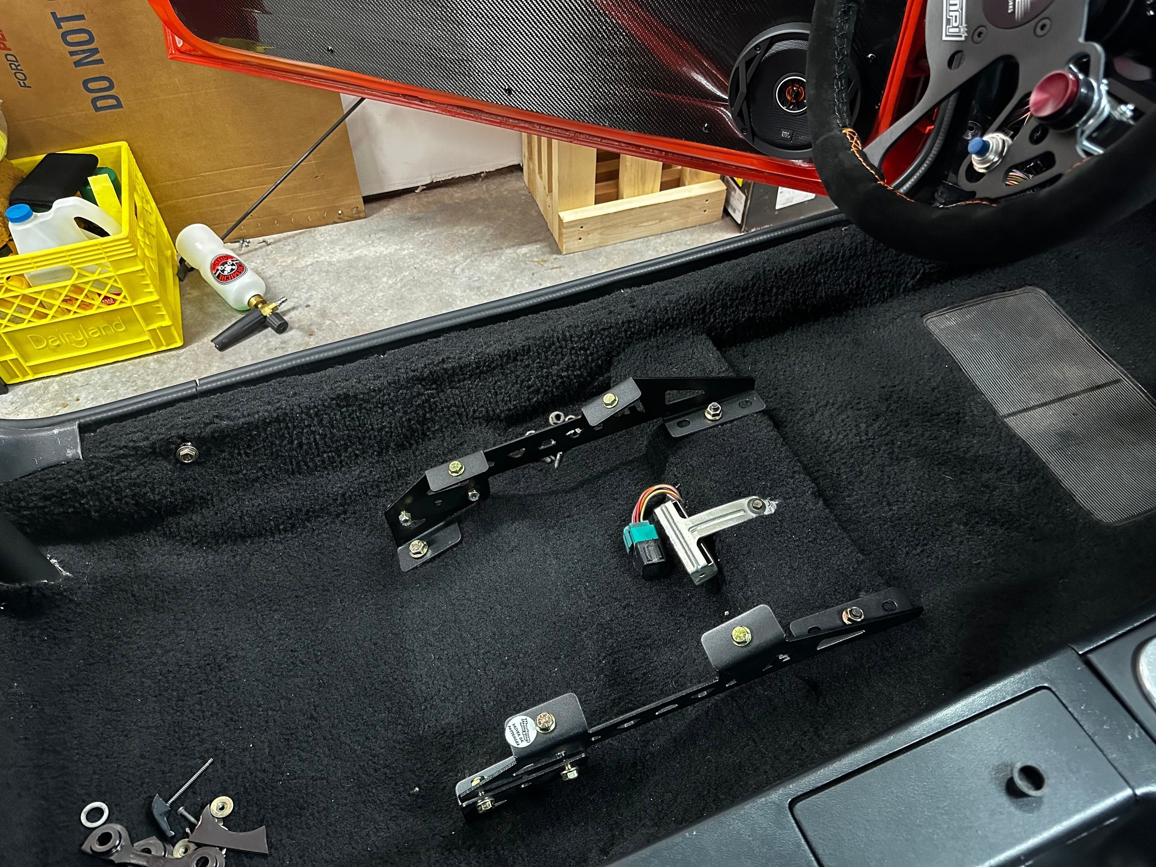 Henderson Race Shop Store black steel seat mount brackets installed on the carpeted floor of a Ford Mustang interior.