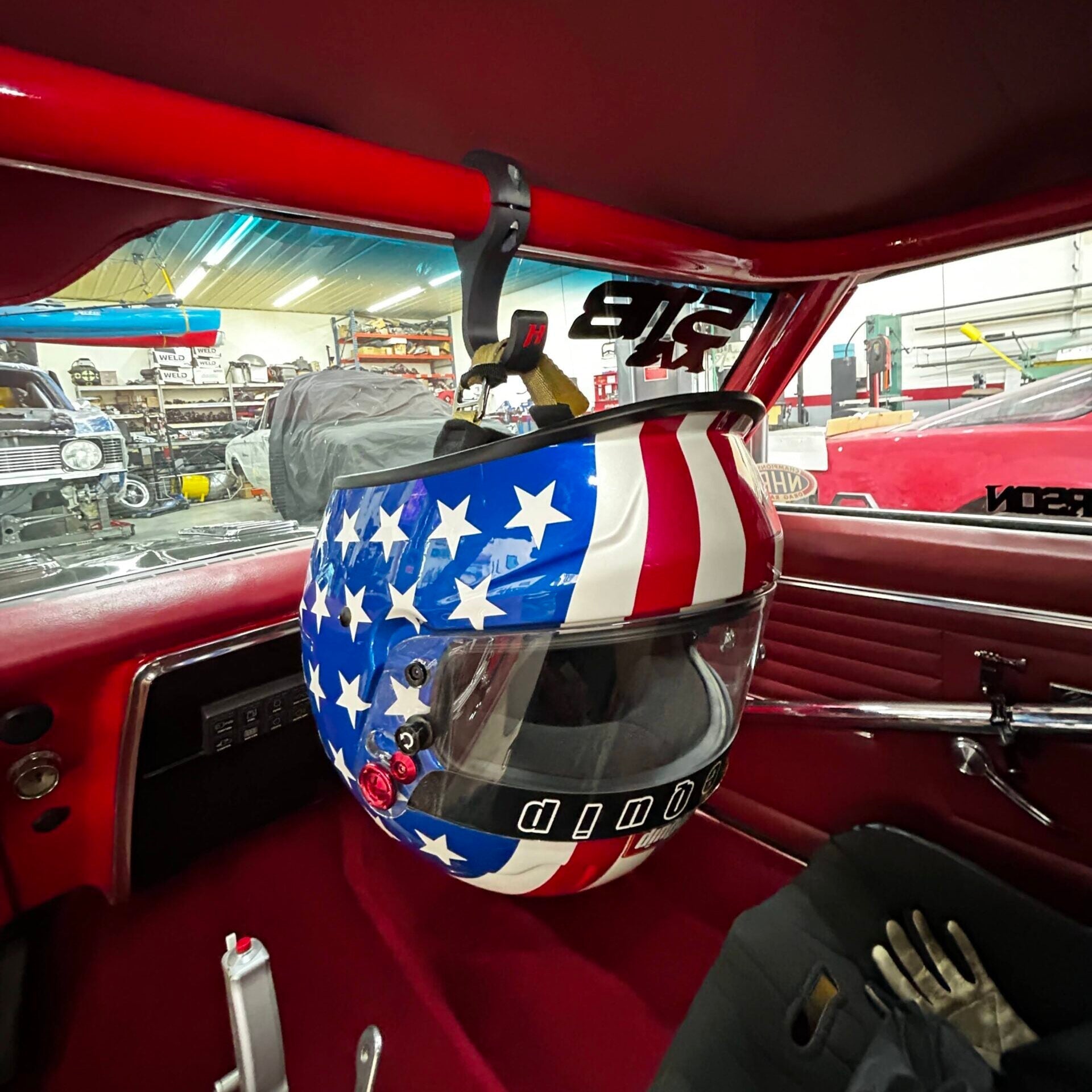 Henderson Race Shop Store heavy duty hook mounting a patriotic helmet to a red roll bar inside a race car cockpit
