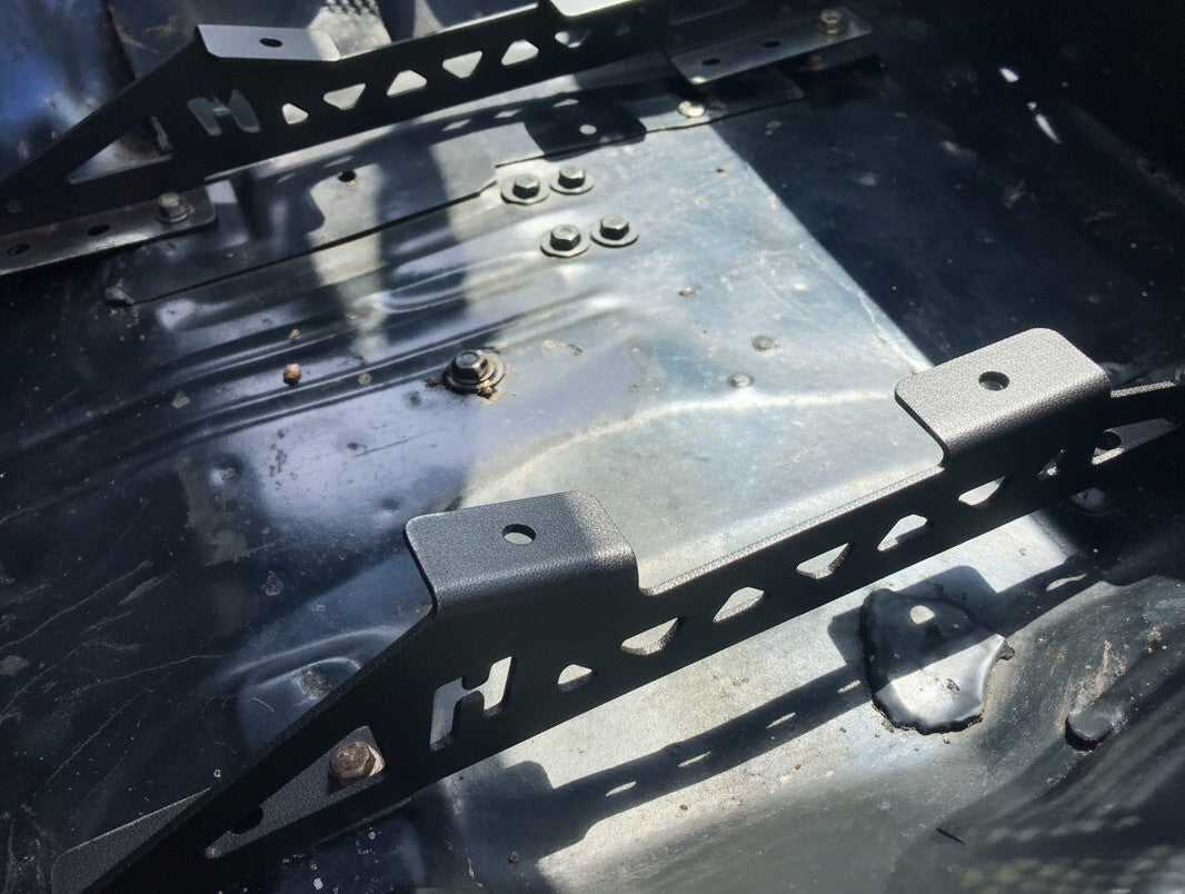 Henderson Race Shop Store black powder-coated steel seat mount brackets installed in a GM A-Body vehicle floor.