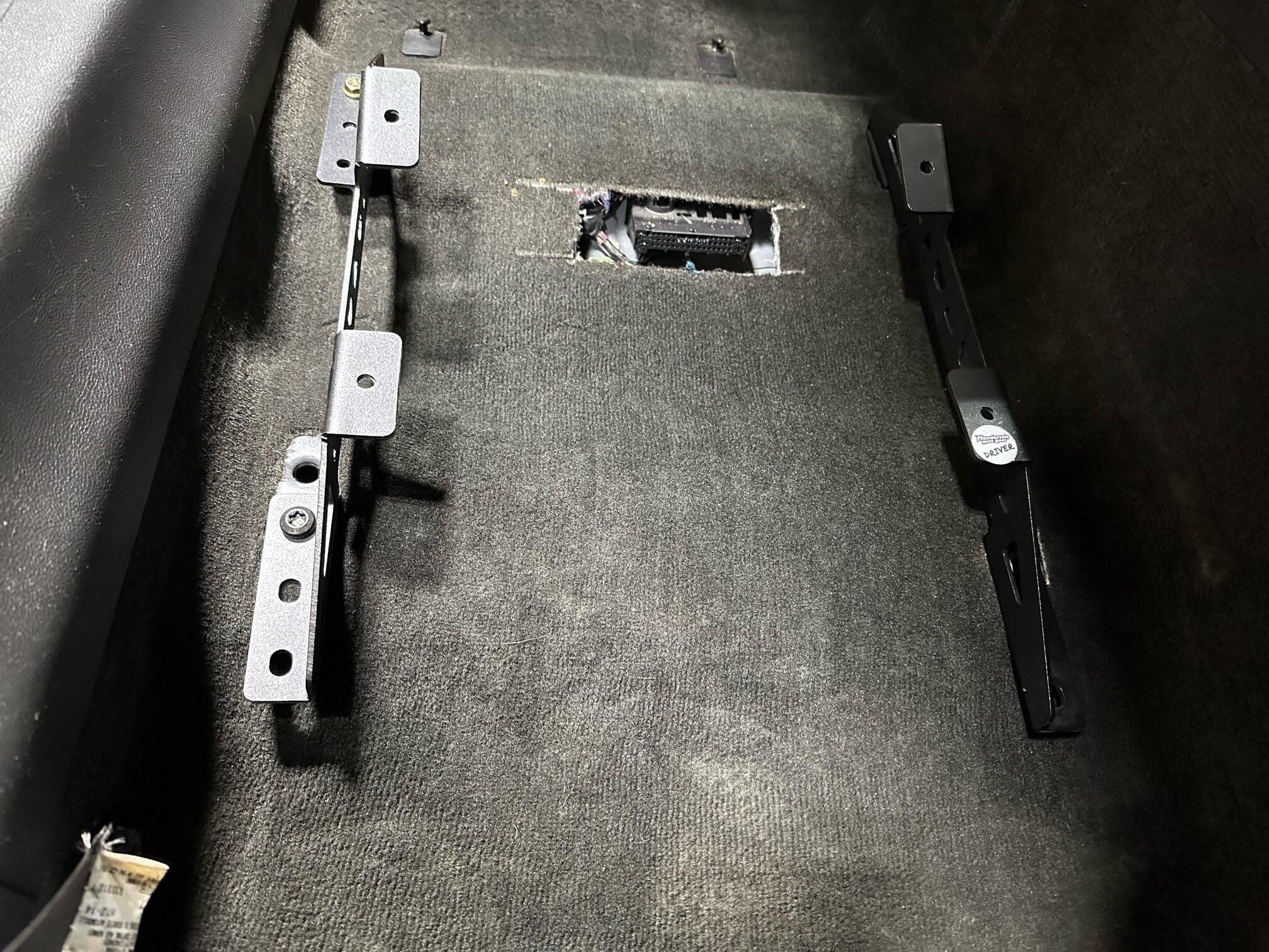 Henderson Race Shop Store black powder-coated steel seat mount brackets installed on a vehicle floor carpet