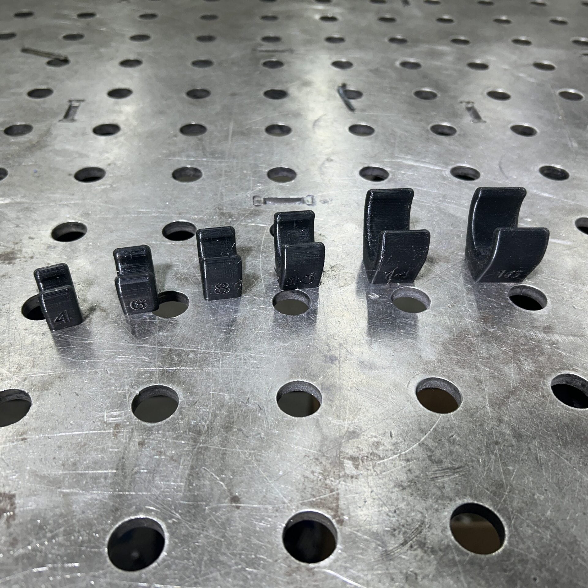 Henderson Race Shop Store black single flat base AN hose clamps in various sizes arranged on a metal welding table.