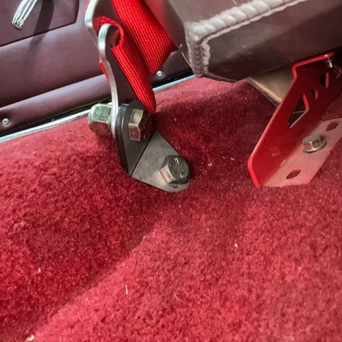 Henderson Race Shop Store black steel 5-point harness floor adapter installed with red racing belt on red carpet