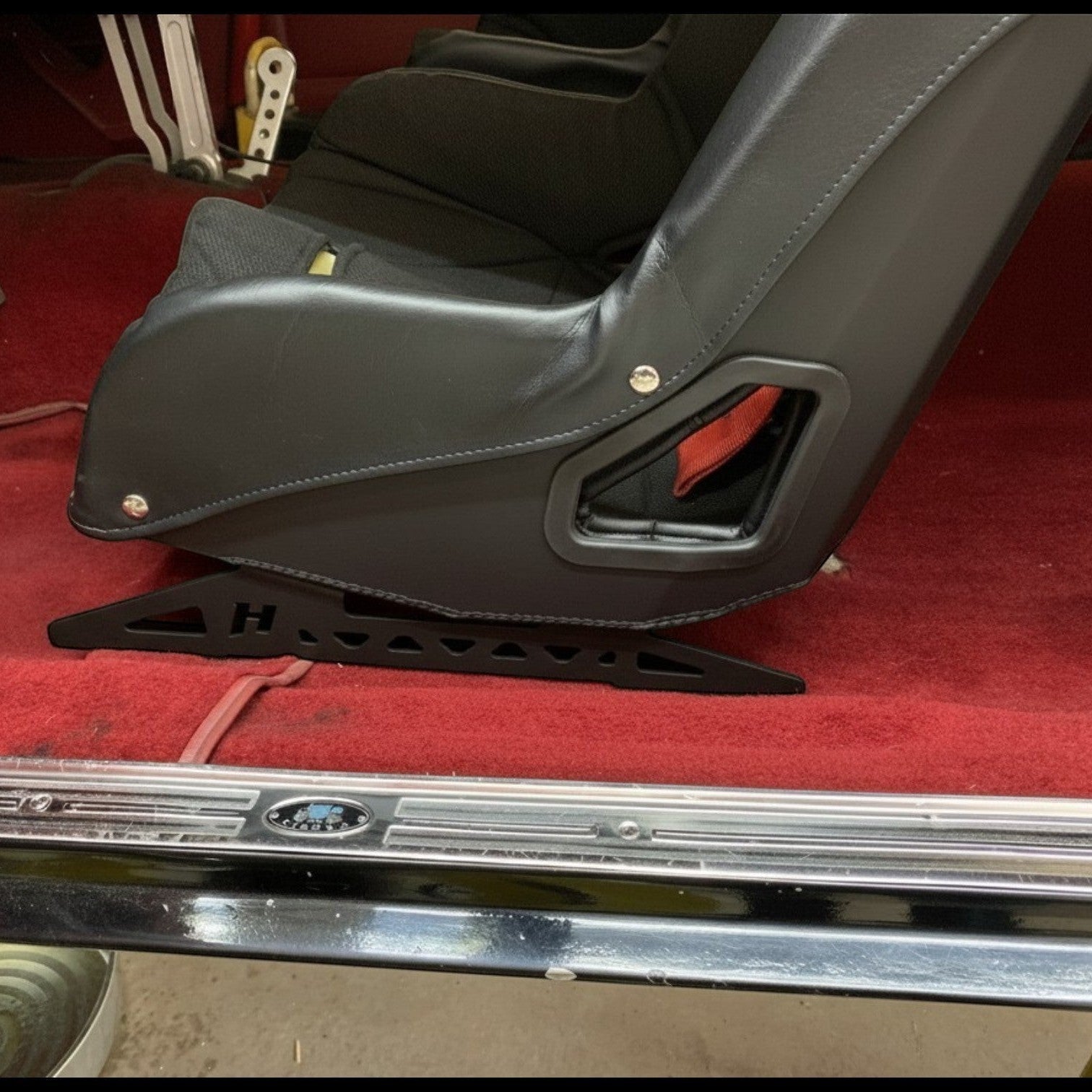 Henderson Race Shop Store black powder-coated steel seat mount bracket installed under a racing seat in a classic car.