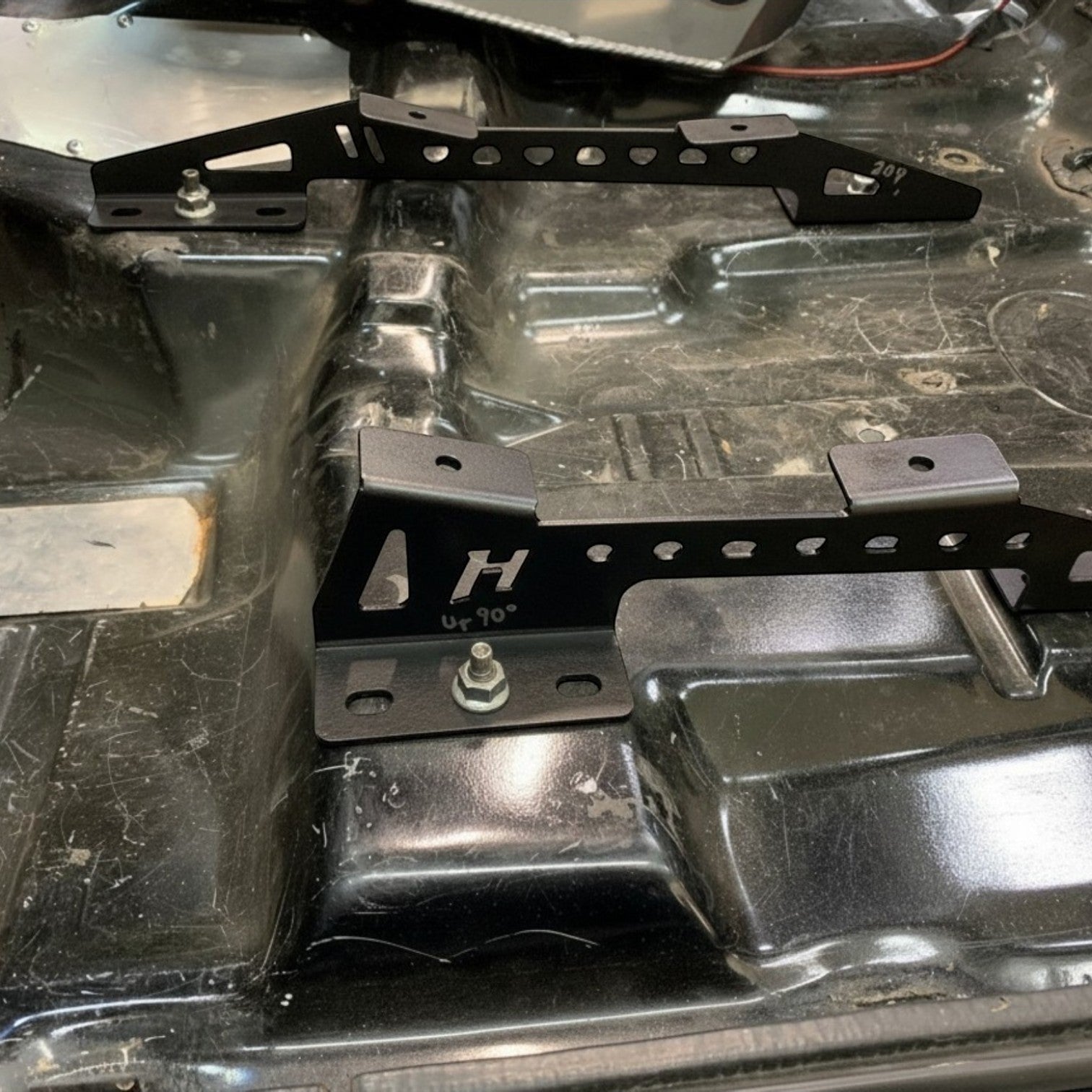 Henderson Race Shop Store black steel seat mount brackets installed on a vehicle floor for Kirkey racing seats.