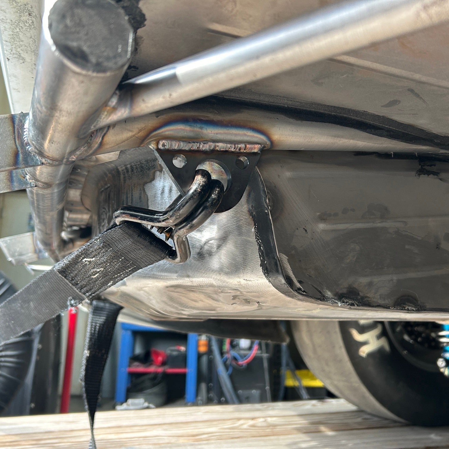 Henderson Race Shop Store weld-on steel tie-down tab welded to a chassis with a black strap attached